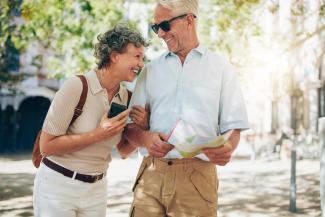 Elderly man and woman laughing. The man is holding a map, and the woman is wearing a backpack. They look like they are travelling.